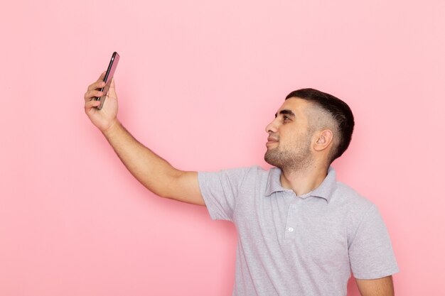 Vue de face jeune homme en chemise grise prenant un selfie sur rose
