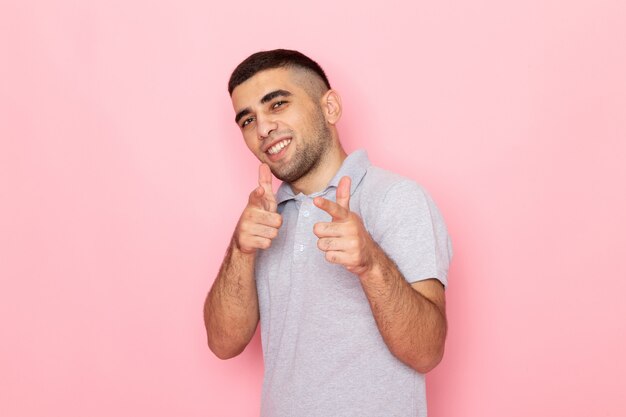 Vue de face jeune homme en chemise grise souriant et drôle posant sur rose