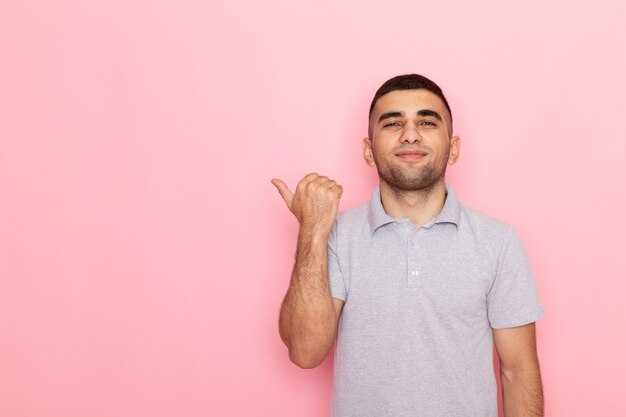 Vue de face jeune homme en chemise grise souriant et montrant avec son doigt sur rose