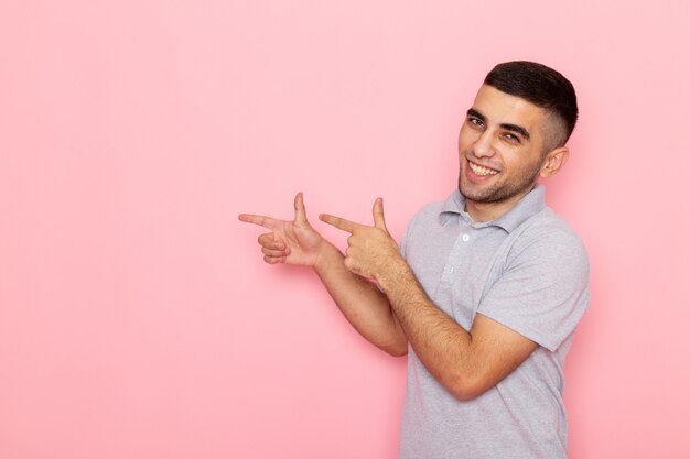 Vue de face jeune homme en chemise grise souriant et soulignant avec les doigts sur rose