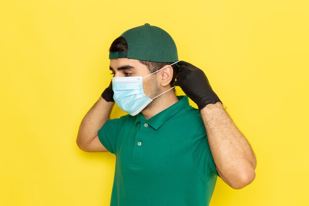 Vue de face jeune homme en chemise verte casquette verte portant un masque stérile sur le fond jaune offrant un travail de couleur de service