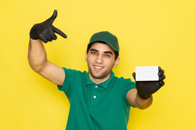 Vue de face jeune homme en chemise verte casquette verte tenant une carte blanche avec des gants noirs sur jaune
