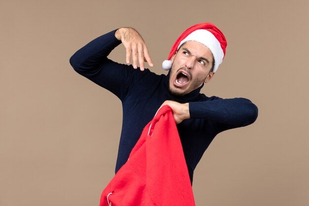 Vue de face jeune homme contrôle présent sac sur fond marron vacances de Noël santa