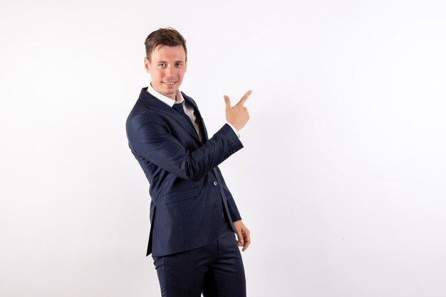 Vue de face jeune homme en costume classique élégant posant avec sourire sur fond blanc