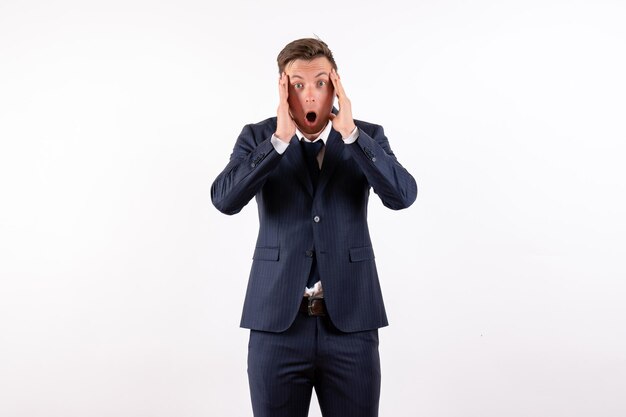 Vue de face jeune homme en costume classique élégant posant avec un visage choqué sur fond blanc