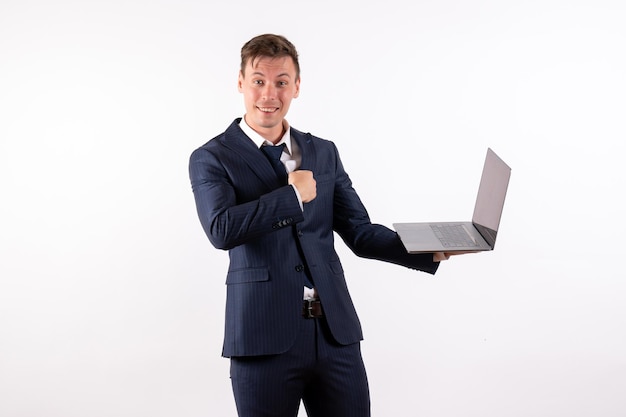 Vue de face jeune homme en costume classique élégant tenant un ordinateur portable sur fond blanc