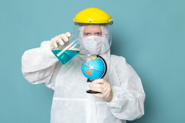 Une vue de face jeune homme en costume spécial blanc et jaune casque spécial holding globe sur le mur bleu homme costume couleur équipement spécial danger