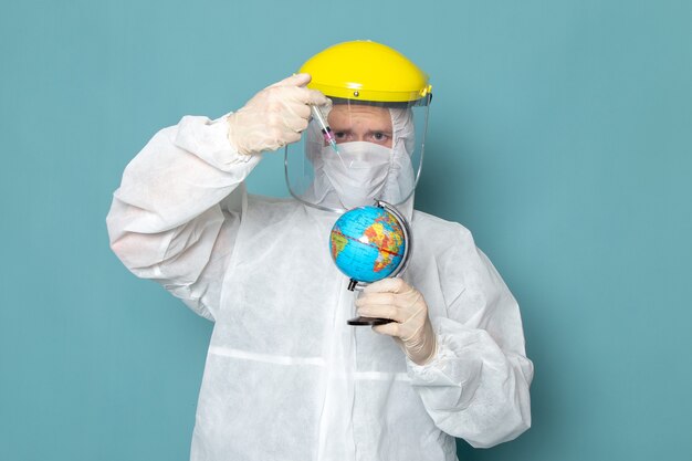 Une vue de face jeune homme en costume spécial blanc et jaune casque spécial injection petit globe sur le mur bleu homme costume couleur équipement spécial danger