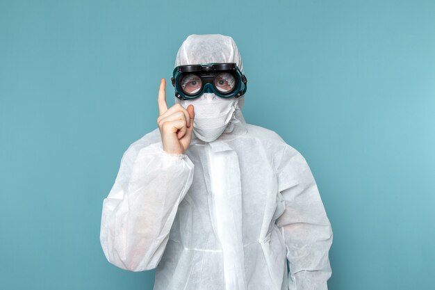 Une vue de face jeune homme en costume spécial blanc portant des lunettes de soleil spéciales menaçant sur le mur bleu homme costume couleur équipement spécial danger