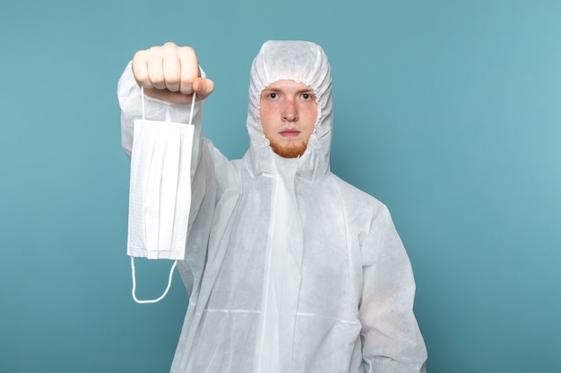 Photo gratuite une vue de face jeune homme en costume spécial blanc portant un masque de protection stérile sur le mur bleu homme costume couleur équipement spécial