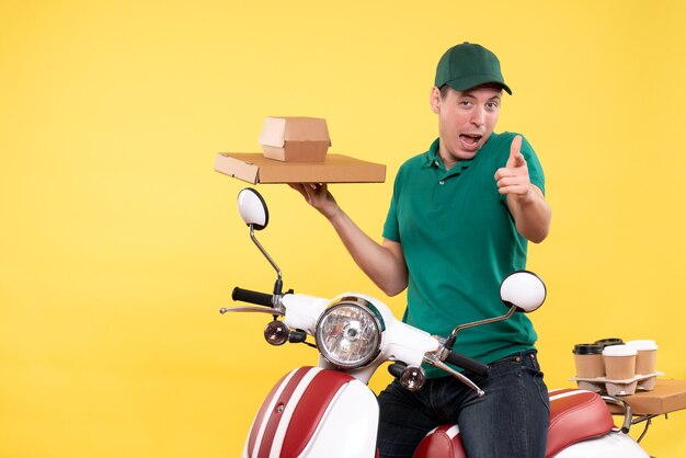 Vue de face jeune homme coursier en uniforme tenant des emballages alimentaires sur jaune