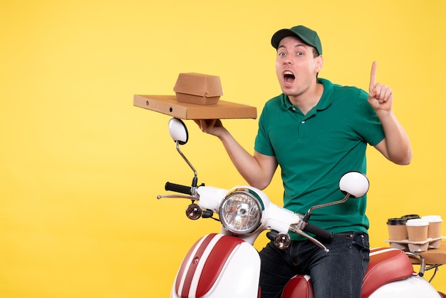 Vue de face jeune homme coursier en uniforme tenant des emballages alimentaires sur jaune