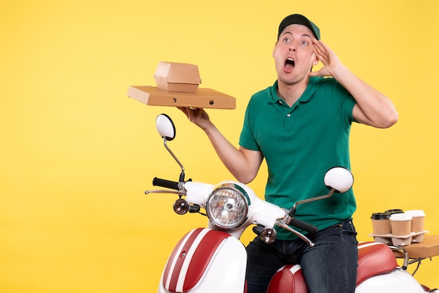 Vue de face jeune homme coursier en uniforme tenant des emballages alimentaires sur jaune