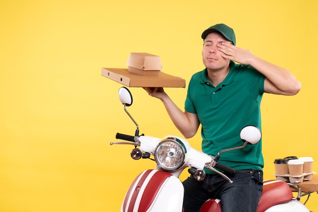 Vue de face jeune homme coursier en uniforme tenant des emballages alimentaires sur jaune