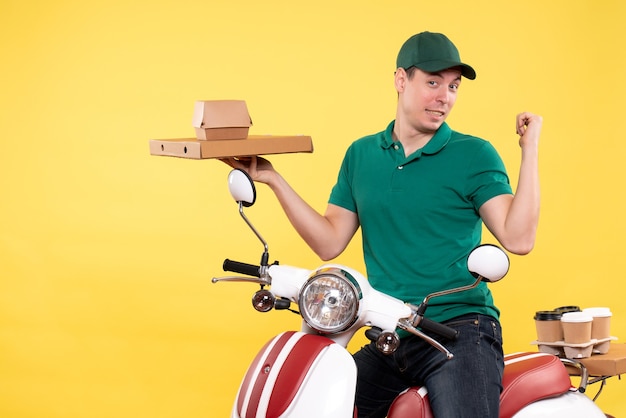 Vue de face jeune homme coursier en uniforme tenant des emballages alimentaires sur jaune