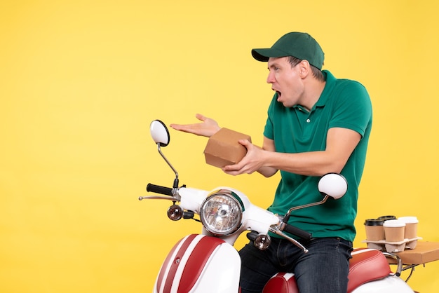 Vue de face jeune homme coursier en uniforme tenant un petit paquet de nourriture sur jaune