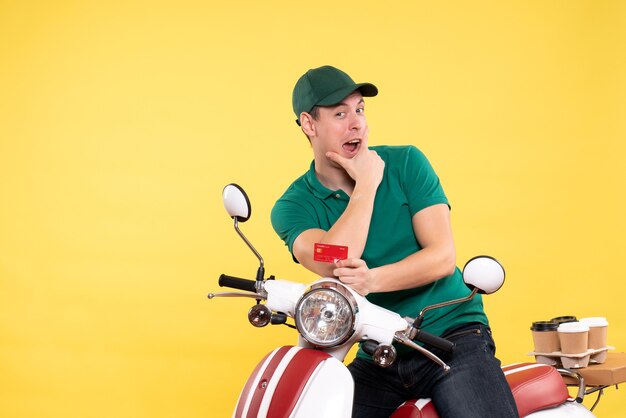 Vue de face jeune homme coursier en uniforme vert tenant une carte bancaire sur jaune