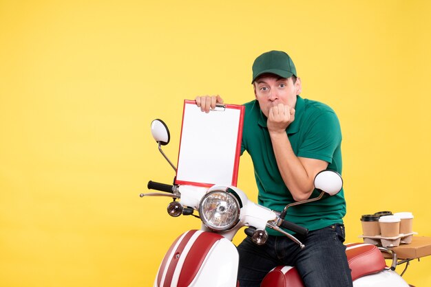 Vue de face jeune homme coursier en uniforme vert tenant une note de dossier sur jaune