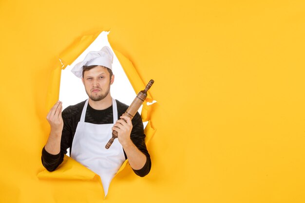 Vue de face jeune homme cuisinier en cape blanche tenant un rouleau à pâtisserie sur fond jaune photo nourriture homme blanc cuisine cuisine travail couleurs