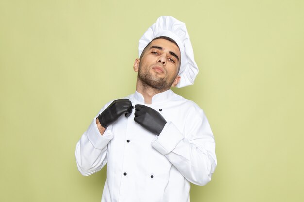 Vue de face jeune homme cuisinier en costume de cuisinier blanc portant des gants noirs sur vert