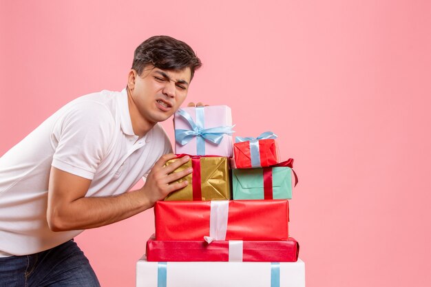Vue de face jeune homme debout autour des cadeaux de Noël sur fond rose