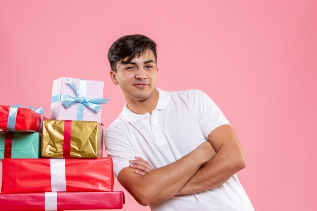 Vue de face jeune homme debout autour des cadeaux de Noël sur fond rose