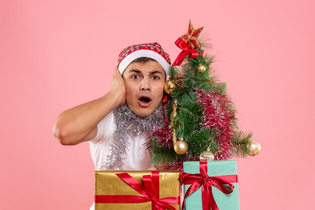 Vue de face jeune homme debout autour des cadeaux de Noël sur fond rose