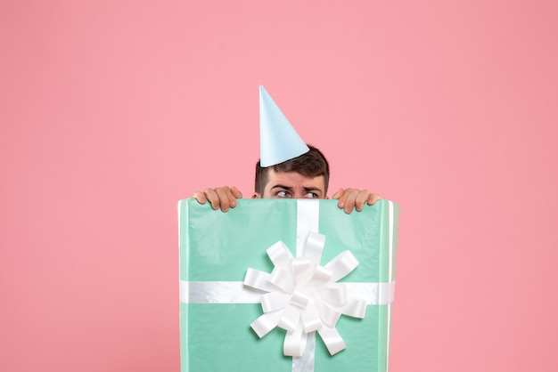 Vue de face jeune homme debout à l'intérieur de la boîte présente sur la couleur rose clair Noël nouvel an photo émotion humaine