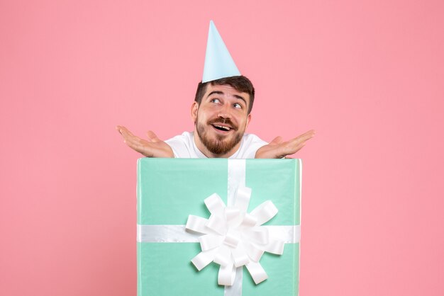 Vue de face jeune homme debout à l'intérieur de la boîte présente sur la couleur rose Noël nouvel an photo émotion humaine