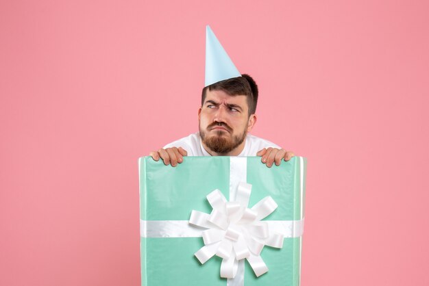 Vue de face jeune homme debout à l'intérieur de la boîte présente sur la couleur rose Noël nouvel an photo émotions humaines