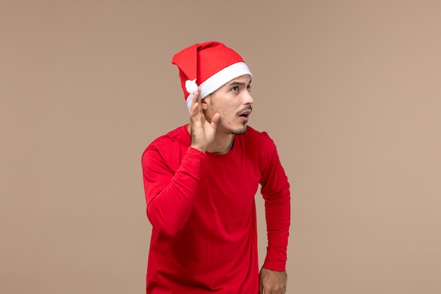 Vue de face jeune homme écoutant attentivement sur fond marron émotion vacances de Noël