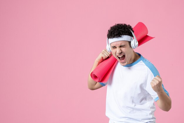 Vue de face jeune homme émotionnel en vêtements de sport avec tapis de yoga