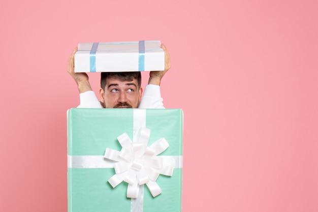 Photo gratuite vue de face jeune homme essayant de se cacher à l'intérieur de la boîte présente sur le jeu de pyjama de sommeil de couleur rose de l'émotion de noël