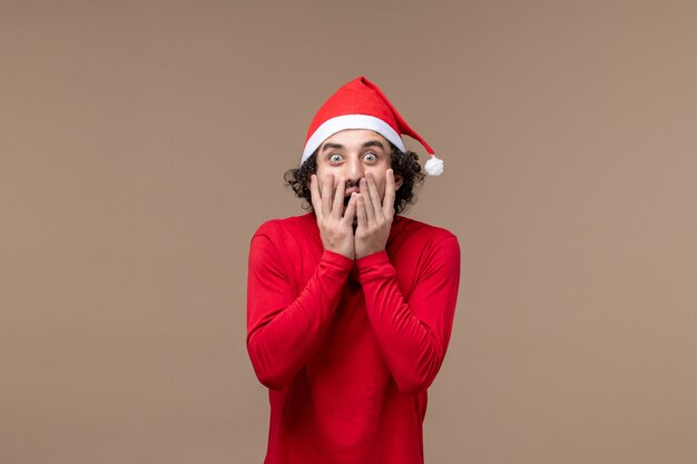 Vue de face jeune homme avec expression choquée sur fond marron vacances d'émotion de Noël