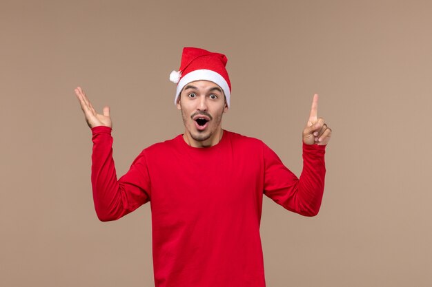 Vue de face jeune homme avec une expression choquée sur plancher brun vacances d'émotion de Noël