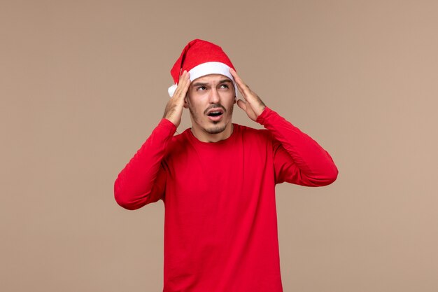 Vue de face jeune homme avec expression confuse sur fond brun émotion de vacances de Noël