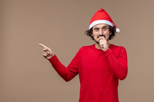 Vue de face jeune homme avec une expression nerveuse sur fond marron vacances Noël émotion
