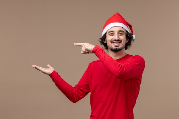 Vue de face jeune homme avec une expression souriante sur fond marron émotion vacances Noël