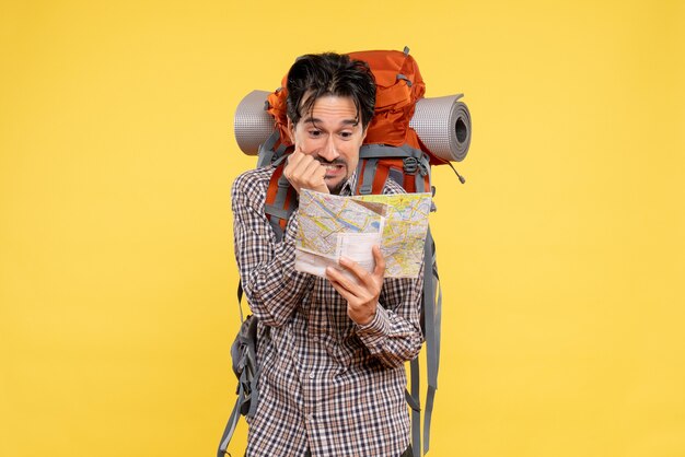 Vue de face jeune homme faisant de la randonnée avec sac à dos observant la carte sur fond jaune voyage d'entreprise campus couleurs de la forêt air