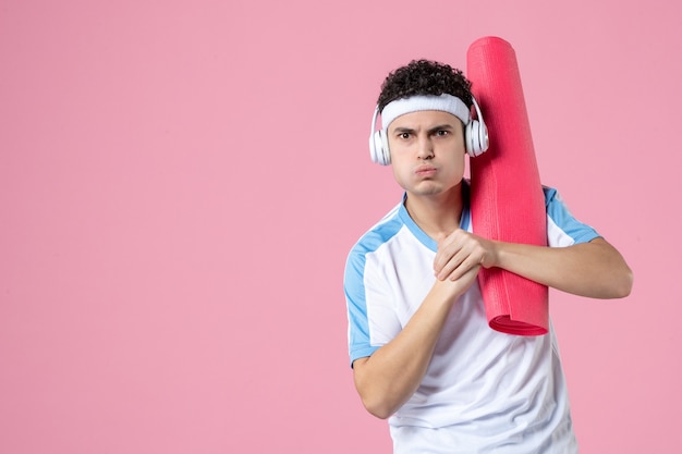 Vue de face jeune homme fort en vêtements de sport avec tapis de yoga