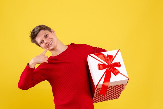 Vue de face jeune homme avec grand cadeau de Noël sur fond jaune