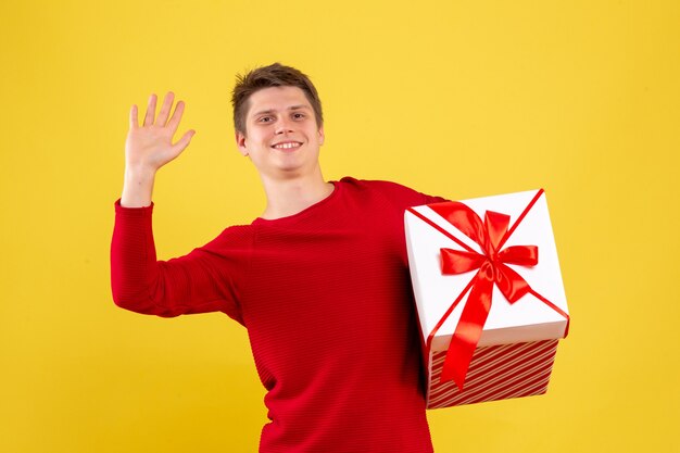 Vue de face jeune homme avec grand cadeau de Noël sur fond jaune