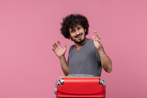 Vue de face jeune homme avec un grand sac rouge se préparant pour un voyage sur un espace rose