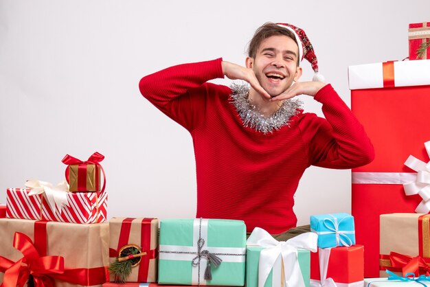 Vue de face jeune homme heureux avec masque assis autour de cadeaux de Noël