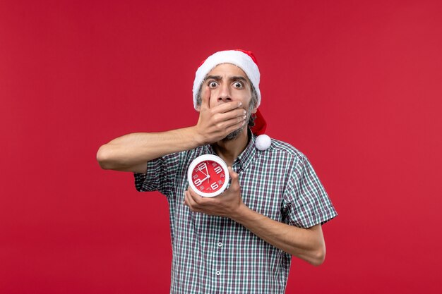 Vue de face jeune homme avec des horloges rondes sur un bureau rouge