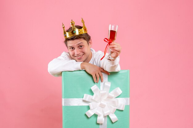 Vue de face jeune homme à l'intérieur présent avec couronne et verre de vin sur fond rose