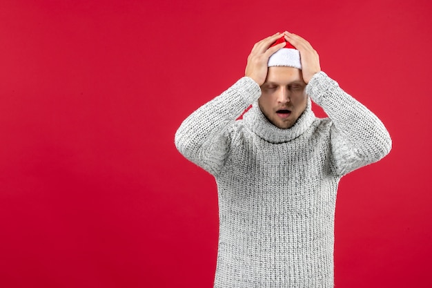 Vue de face jeune homme en jersey chaud fatigué sur fond rouge