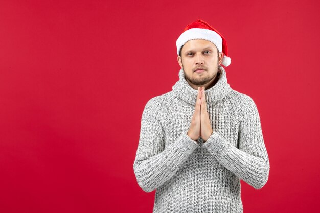 Vue de face jeune homme en jersey chaud priant sur fond rouge