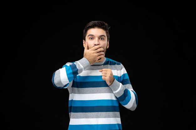 Vue de face jeune homme en jersey rayé bleu choqué sur le mur noir