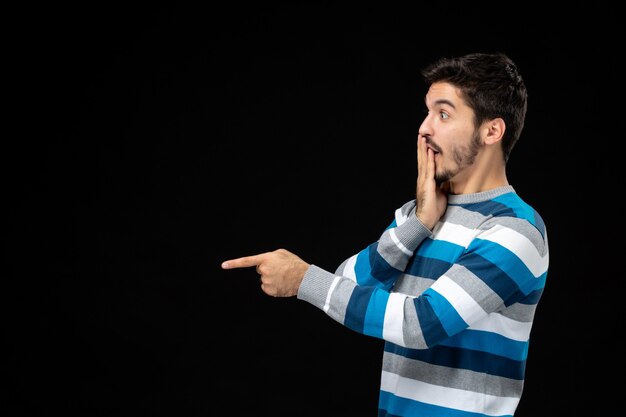 Vue de face jeune homme en jersey rayé bleu sur mur noir modèle photo couleur obscurité